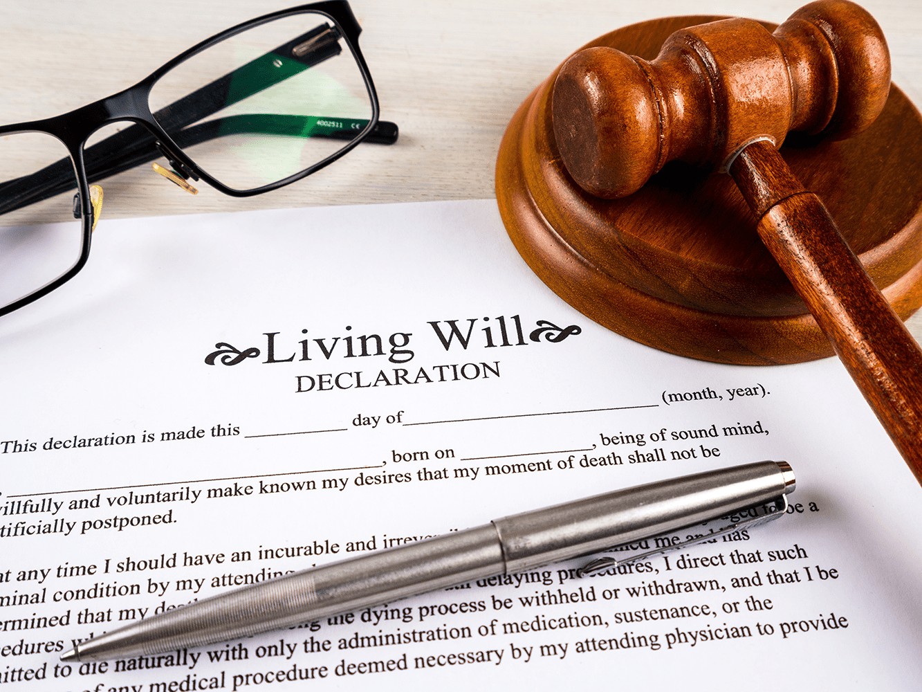 Living will declaration form with pen, gavel and striking block and glasses on top.