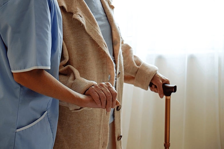 Senior woman holding quad cane handle in elderly care facility.
